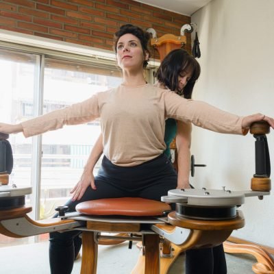 Female teacher teaching her female student correct technique of exercising on rehabilitation machine to strengthen and improve joint health.